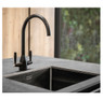 Caple Avel kitchen tap in black installed over a black sink and grey worktop, with a garden backdrop
