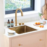 Caple Mode 45cm sink in gold installed with gold tap, featuring dish soap, stacked plates, and orang