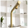 Agilis Single Lever Kitchen Tap by Abode in a brass finish against blurred kitchen shelf background