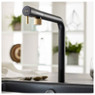 Abode Agilis Single Lever Kitchen Tap in black with brass accents over a sink in a bright kitchen