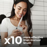 Woman brushing with Aeno DB1S Smart Toothbrush while checking smart app on her phone.