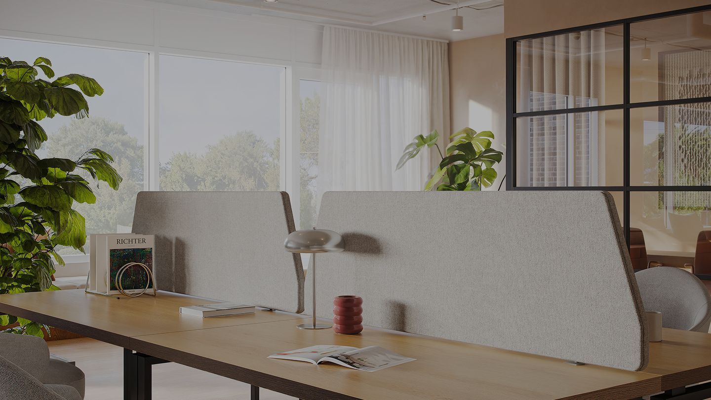 Light grey fabric acoustic desk screens on long bench desks in a bright open-plan office