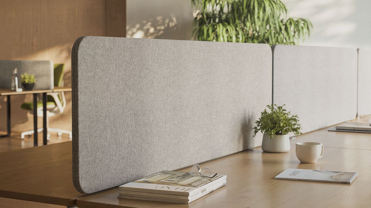 Grey fabric desk screens with rounded corners on wooden office desks in a bright open-plan office