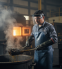 Industrial worker wearing 18-inch Neoprene Chemical Handling Gloves with a rough grip, apron, and face shield, safely retrieving hot, oily parts from a chemical immersion tank in a heat-treating or manufacturing facility.