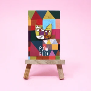 Enamel pin of multicolored Paul Klee-esque cat on tiny easel.