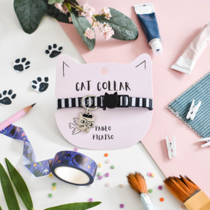 Black and white striped cat collar featuring silver cat charm on cat-shaped backing card. Black and white striped cat collar featuring silver cat charm on cat-shaped backing card.
