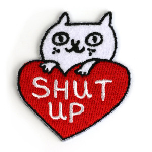 White cat holding a red heart patch, text: shut up White cat holding a red heart patch, text: shut up