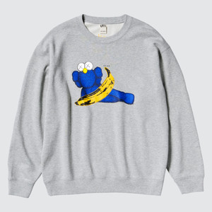 Grey crewneck sweatshirt, KAWS Blue BFF, laying down sideways, holding a yellow Warhol banana. Grey crewneck sweatshirt, KAWS Blue BFF, laying down sideways, holding a yellow Warhol banana.