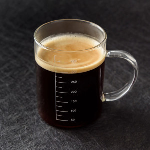A glass mug with metric measurements on the side filled with black coffee