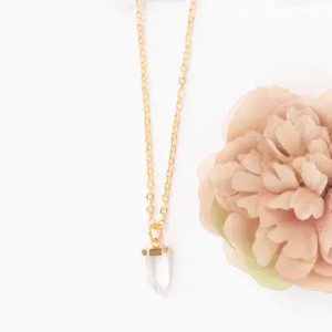 A quartz crystal pendant suspended on a gold chain next to a beige carnation A quartz crystal pendant suspended on a gold chain next to a beige carnation