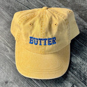 pigment dyed yellow baseball cap, blue embroidered text "butter"