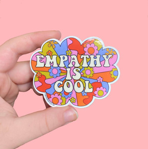 A hand the sticker, white lettering "empathy is cool"on a flower power style background. A hand the sticker, white lettering "empathy is cool"on a flower power style background.
