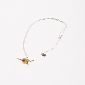 necklace laid flat. the pendant is a silver oval with a 3D golden diplodocus fossil on it. necklace laid flat. the pendant is a silver oval with a 3D golden diplodocus fossil on it.