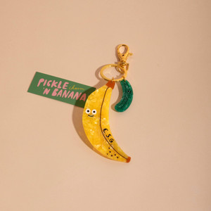 Banana shaped flat charm attached to key ring and a smaller pickle shaped charm. Banana shaped flat charm attached to key ring and a smaller pickle shaped charm.