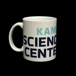 A white porcelain mug with the first half of the Kamin Science Center Logo visible