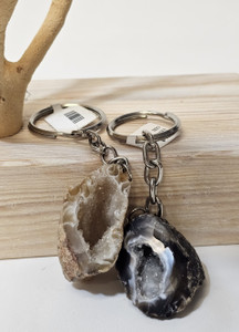 Two half geode keychains, one tan, and one black and tan, set against a wooden base.