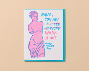 Note card features pink Aphrodite statute with Blue text that reads " Mom you are a" Pink text with a slash through " Piece of work" and Blue text " Work of art."  To be read as " Mom you are a piece of art."
