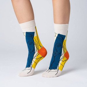 Abstract socks featuring line drawn faces and the colors yellow, blue, and orange -- Photographed worn on feet.