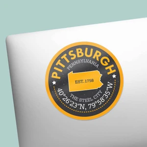Round sticker with Black background and bold gold trim. Artwork features state of Pennsylvania in gold with a text that reads "Est. 1758." Bottom of sticker has white text that reads "Steel City" featuring Pittsburgh's coordinates.