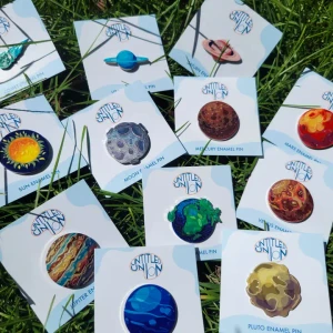 An assortment of enamel pins featuring illustrations of the Sun, eight planets, Pluto, and a comet