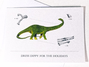 Greeting card with Diplodocus "Dippy" dinosaur in center of card, with scarf, hat and skies balanced on the border and the text "Dress Dippy for the Holidays" centered at the bottom of the card. Greeting card with Diplodocus "Dippy" dinosaur in center of card, with scarf, hat and skies balanced on the border and the text "Dress Dippy for the Holidays" centered at the bottom of the card.