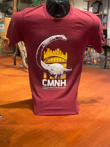 Photo of the red (tone is comparable to brick or burgundy) variant of the bridge shirt. Dippy, highlighted in white, stands in front of a yellow silhouette featuring an iconic Pittsburgh bridge as well as the city skyline. Large white text reading "CMNH" sits below. Beneath this, in a smaller font, "Carnegie Museum of Natural History" and "Pittsburgh" are printed.