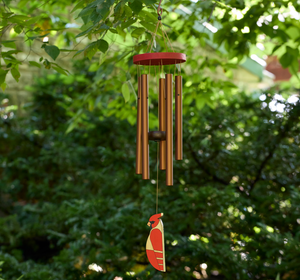Picture of windchime hanging. Warm cord connects bronze colored tubes to a central hook, while a painted cardinal acts as the wind sail. The wooden top of the windchime is red like the cardinal.
