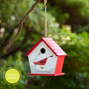 Image shows birdhouse hanging. Sides and roof are a bright red, while the 1954 "Cardinal with Berries" illustration of a  bright red cardinal perched among angular, stark branches while consuming vibrant clusters of berries in the "minimal realism" and geometric style Charley Harper was known for is painted on the front.