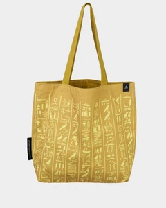 The front of the tote. It is a warm, sandy gold, with the hieroglyphs in a lighter yellow. They cover the entirety of the bag. The inner fabric is the same yellow as the hieroglyphs.