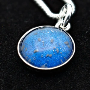 A pendant with lunar dust contained in glass against a blue background