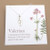 shows silver necklace with silver amulet engraved with a valerian plant on a white backing card with a larger valerian image on it