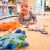 A baby playing with three slat plush planet-themed sensory toys during tummy time