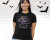 A woman wearing a black t-shirt with the words "Welcom to the Dark Side of Science" surrounded by images of scary science like skeltons, black holes, and poison