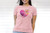 A woman wearing a pink Science Mom t-shirt in front of a white paneled background