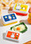 Image of Miffy food containers filled with food and arranged with dishes on table.