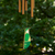 Picture of windchime hanging. Warm cord connects bronze colored tubes to a central hook, while a painted hummingbird acts as the wind sail. The wooden top of the windchime is green like the hummingbird.