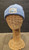 A photo of the powder blue beanie on a mannequin. The knit texture is visible. Centered on the cuff is a silver patch bearing the CMNH Logo. This includes text reading "CMNH" and "Established 1895" above and flanking the silhouette of Dippy, the CMNH logo, in light blue. "Carnegie Museum of Natural History" is written below this.