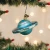 A blown-glass ornament in the shape of the planet Uranus hanging off a Christmas tree