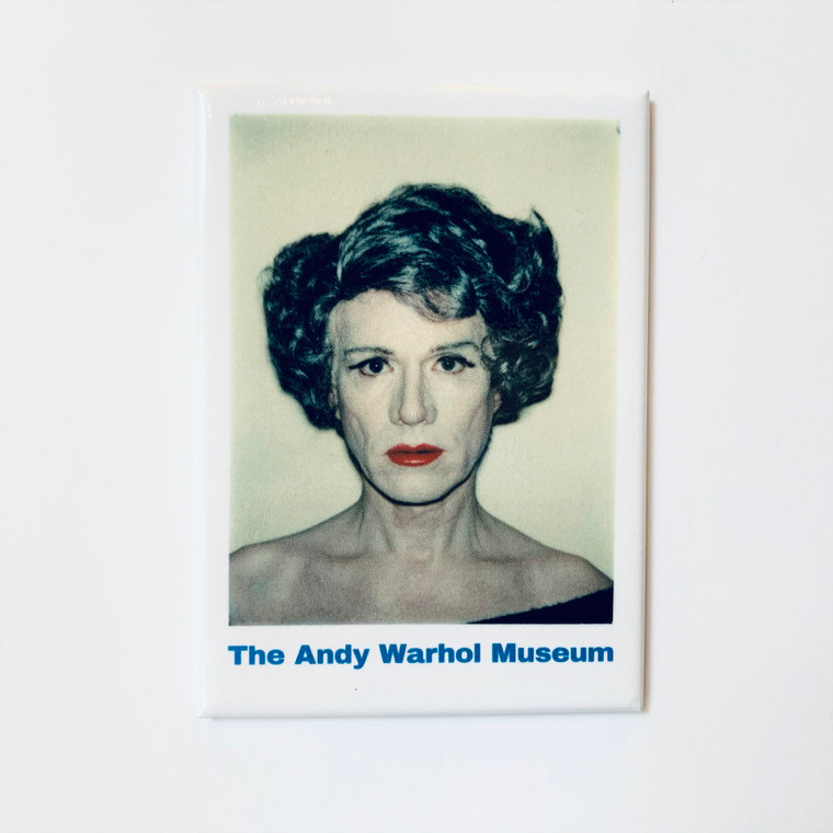 Image of a white rectangular magnet with a dark portrait of Andy Warhol, looking stoic in a wig for a woman, white makeup and red lipstick. The bottom of the magnet reads The Andy Warhol Museum in blue text.