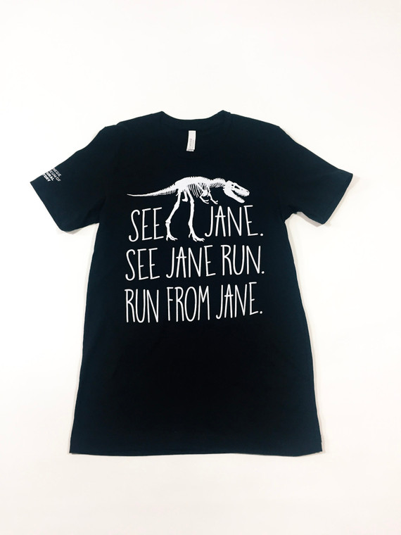 Black youth t-Shirt imprinted in white with a full front Tyrannosaurs Rex fossil sandwiched between the text See Jane, See Jane Run, Run from Jane,  with the Carnegie Museum of Natural History logo on the right sleeve.