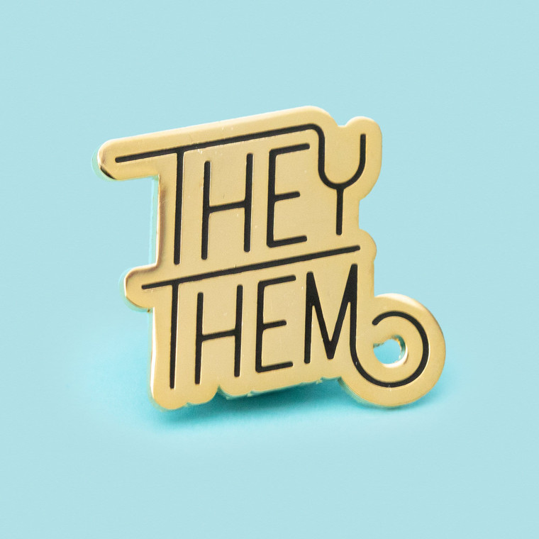 they/them pin in gold and black.