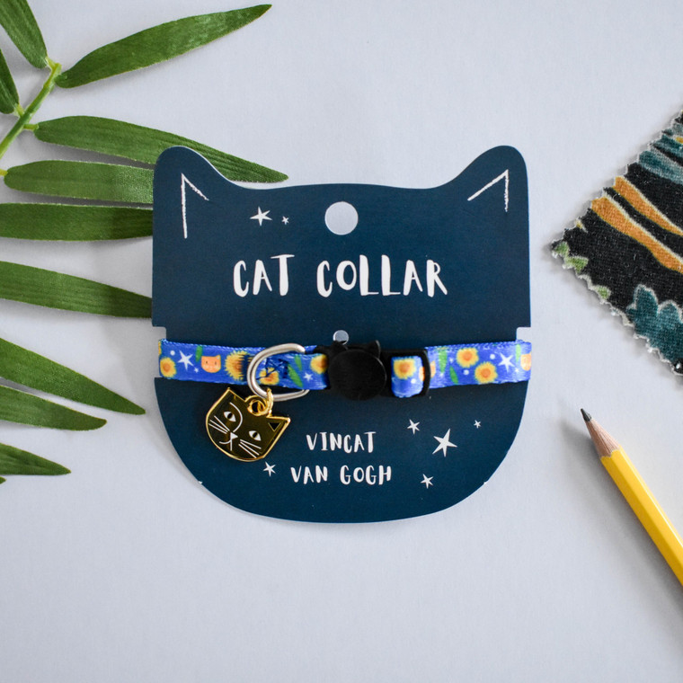 Bright blue cat collar featuring sunflowers, stars, and a brown cat with one ear.  Cat- shaped metal charm and black buckle.