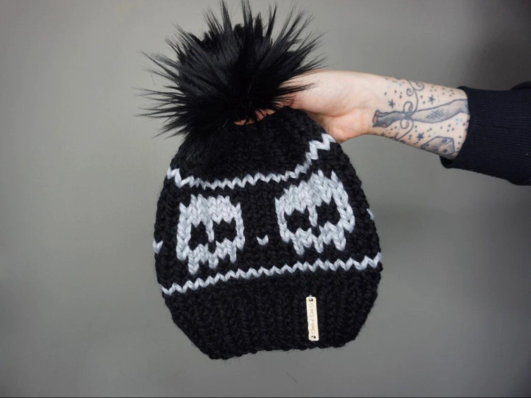 Black knitted beanie with white yarn skull accents.