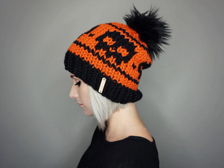 Orange and black knit beanie with black faux fur pom.