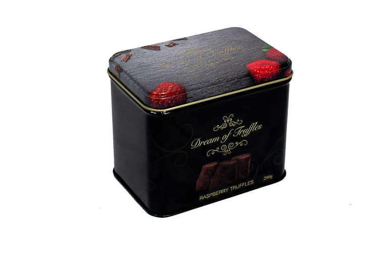 black tin with "dream of Truffles" printed on lid & front in gold script. front of tin has picture of truffles, lid has pictures of raspberries lower right corner