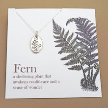shows silver necklace with silver amulet engraved with a fern on white backing card with a larger fern image on it