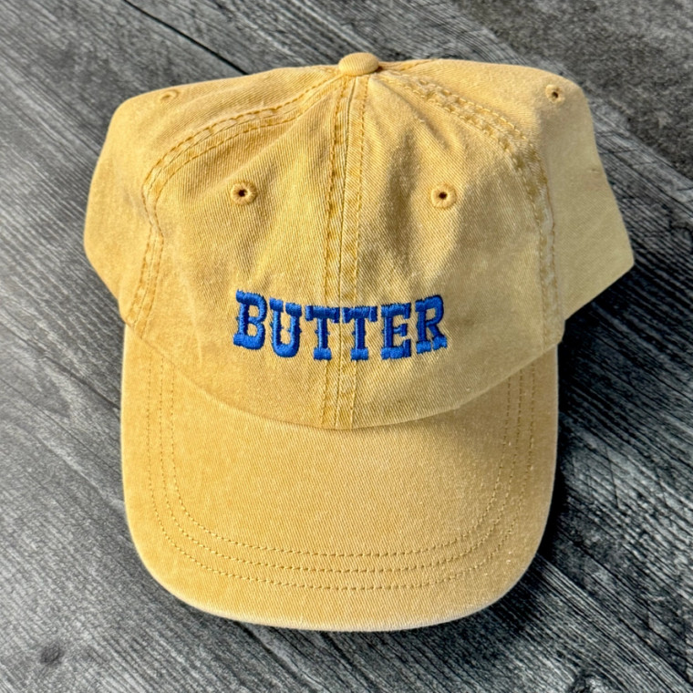 pigment dyed yellow baseball cap, blue embroidered text "butter"