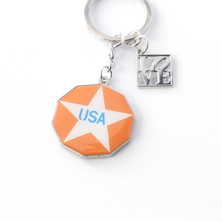 One side of the New Glory penny keychain, white star on an orange background, txt says USA, on a silver keyring.