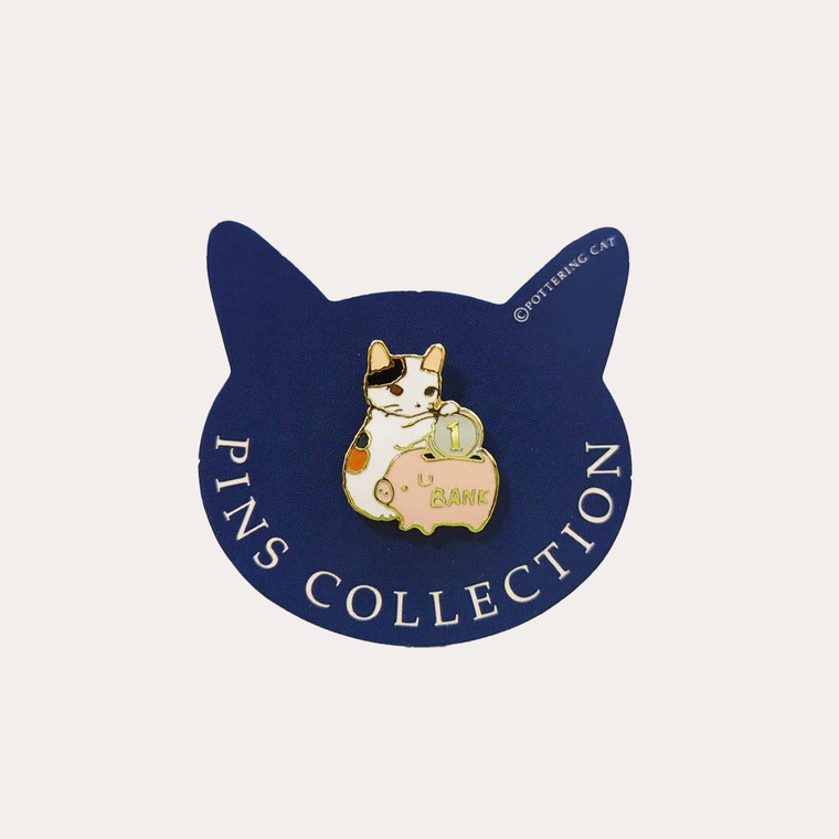 Blue cat head shaped paper backing card, enamel pin of cat and a piggy bank.