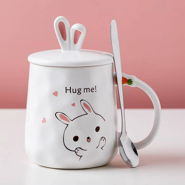 white bunny on a white mug reading "hug me!" the lid has rabbit ears